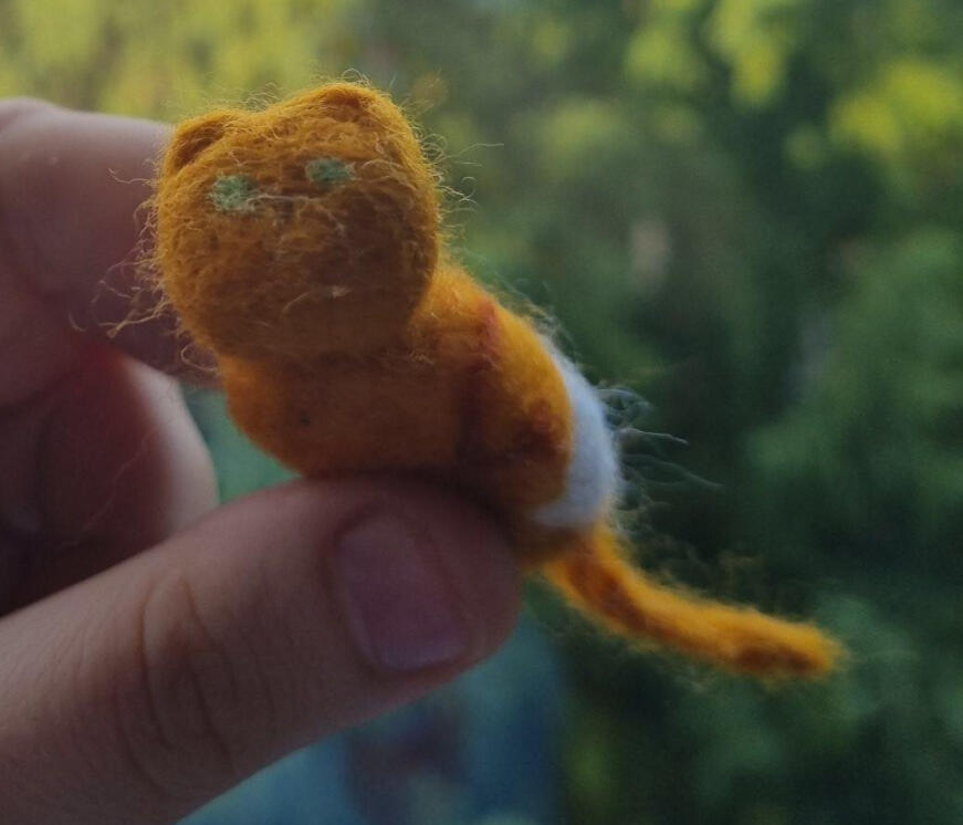 Close-up of a hand holding a very small orange and white needle felted cat